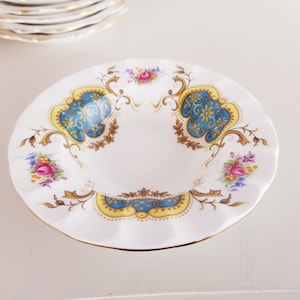 Puede incluir: Un platillo de cerámica blanca con un borde festoneado y un diseño floral azul y dorado. El platillo tiene un borde rizado y un borde dorado.