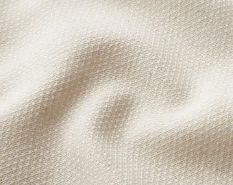 May include: Close-up of a textured, off-white fabric. The weave is visible, creating a subtle pattern of diagonal lines. The fabric has a soft, slightly rumpled appearance, suggesting a natural fibre textile.