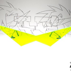 Puede incluir: Un par de gafas de sol triangulares amarillas con brazos verdes. Las gafas de sol est&aacute;n delante de un dibujo de dos personajes de anime.