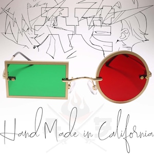 Könnte beinhalten: Goldfarbene Sonnenbrille mit einem rechteckigen grünen Glas auf der linken Seite und einem runden roten Glas auf der rechten Seite. Die Sonnenbrille ist handgefertigt in Kalifornien.