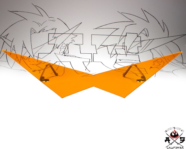 Puede incluir: Visera de pl&aacute;stico naranja con dos clips de metal dorado. La visera tiene forma de alas. La visera est&aacute; delante de un dibujo de dos personajes de anime.