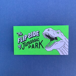 May include: Green rectangular sticker with the text "The Flip Side of Jurassic Park" in black and white lettering. A white cartoon dinosaur with an open mouth is on the right side of the sticker.