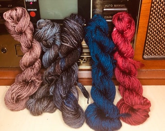 May include: Four skeins of yarn in different colors: a dusty rose, a dark grey with blue flecks, a dark blue with green flecks, and a deep red.