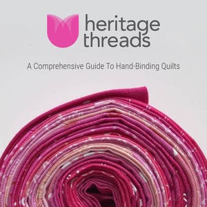 Könnte beinhalten: Nahaufnahme einer rosa-weißen Stoffbinde-Rolle zum Quilten. Der Stoff ist fest aufgerollt und hat ein dezentes Muster. Die Rolle ist mit "heritage threads" und "A Comprehensive Guide To Hand-Binding Quilts" beschriftet.