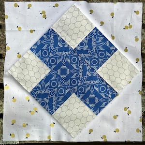 May include: A white fabric square with a blue and white patterned square in the center. The blue and white patterned square is made up of four smaller squares, each with a different pattern. The fabric is decorated with small gold dots.