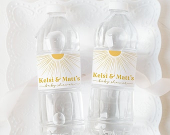 May include: Two clear plastic water bottles with personalized labels for a baby shower. The labels feature a yellow sun with rays and the text "Kels & Matt's Baby Shower".