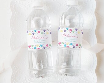 Könnte beinhalten: Zwei durchsichtige Plastikwasserflaschen mit personalisierten Etiketten. Die Etiketten sind weiß mit rosa Rand und zeigen ein buntes Herzmuster. Der Text auf den Etiketten lautet "Addison's Baby Shower".