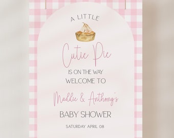 May include: A pink and white gingham background with a white archway. The archway has a pink and white illustration of a pie with the text "A Little Cutie Pie is on the way. Welcome to Maddie & Anthony's Baby Shower. Saturday April 08."