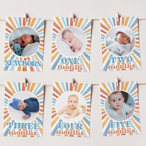 May include: A set of six baby milestone cards, each featuring a photo of a baby and the month. The cards are decorated with a retro sunburst design in orange, blue, and white, and are clipped to a string.