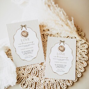 May include: Two bridal shower invitations with a coffee cup design and the text "Love is brewing." The invitations have a striped background and are decorated with a bow. The invitations are on a woven placemat.
