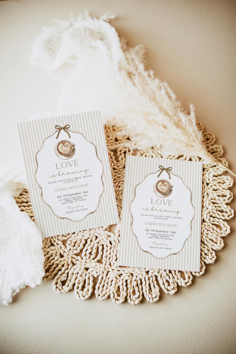 May include: Two bridal shower invitations with a coffee cup design and the text "Love is brewing." The invitations have a striped background and are decorated with a bow. The invitations are on a woven placemat.