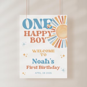 May include: A rectangular sign with the text "ONE HAPPY BOY" in blue and orange, with a watercolor sun illustration. The sign reads "WELCOME TO Noah's First Birthday" and the date "APRIL 08 2026".