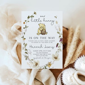 May include: A Winnie the Pooh themed baby shower invitation with a floral wreath and a bee. The text reads "our little hunny is on the way".