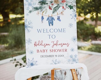 May include: A baby shower welcome sign on a wooden easel. The sign features snowflakes, greenery, and baby clothes illustrations. Text reads "Welcome to Addison Johnson's Baby Shower, December 19 20XX."