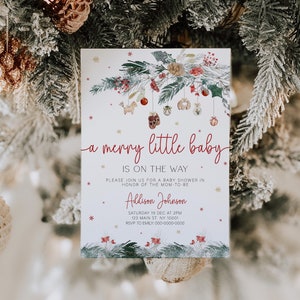 May include: A white baby shower invitation featuring a watercolour illustration of a wintery pine branch adorned with ornaments and a red and white striped bow. The text reads "a merry little baby is on the way" and includes the name "Addison Johnson", date, time, location, and RSVP details.
