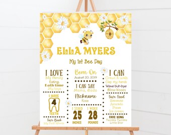 May include: A white and yellow printable baby milestone poster with a bee theme. The poster features a cartoon bee, honeycomb, and daisies. The text on the poster reads "Ella Myers, My 1st Bee Day". The poster includes information about the baby's age, weight, height, favourite foods, and songs.