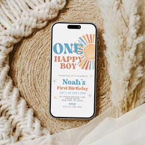 May include: A smartphone displays a birthday invitation with the text "ONE HAPPY BOY" and "Noah's First Birthday." The design features a sun graphic and a retro color scheme. The phone rests on a textured surface.