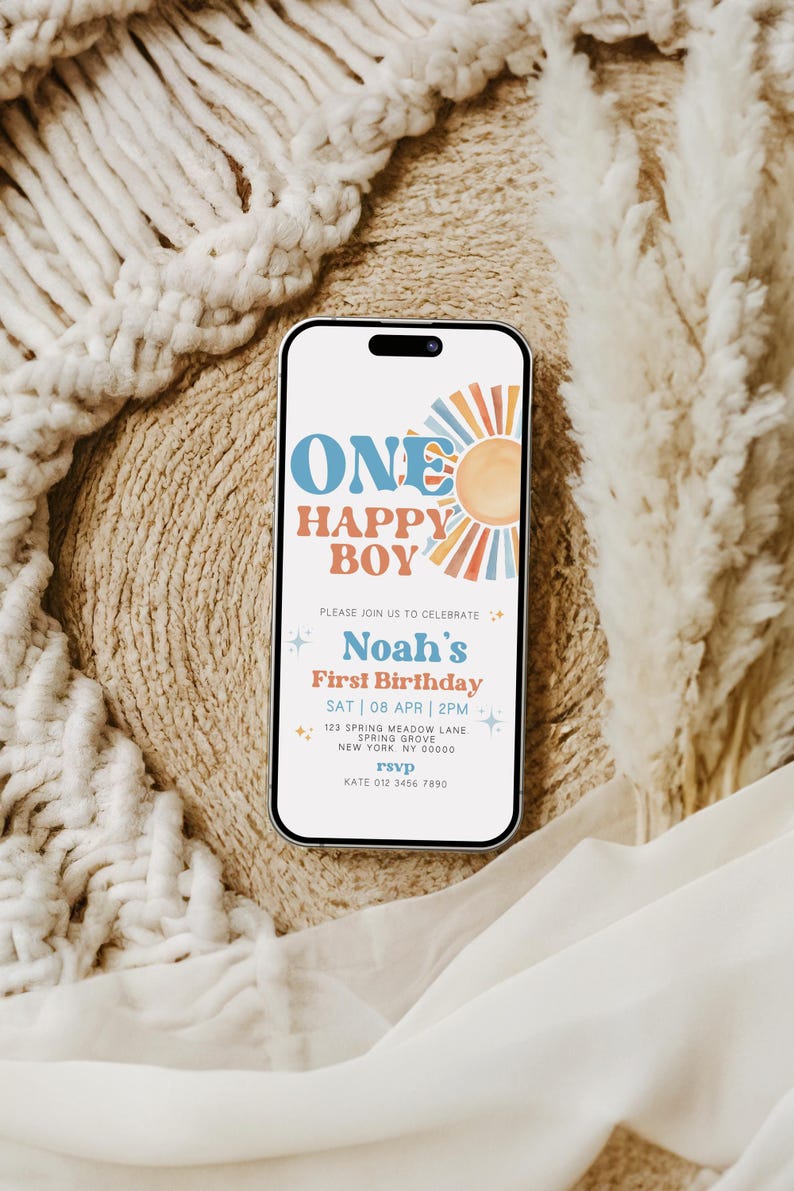 May include: A smartphone displays a birthday invitation with the text "ONE HAPPY BOY" and "Noah's First Birthday." The design features a sun graphic and a retro color scheme. The phone rests on a textured surface.