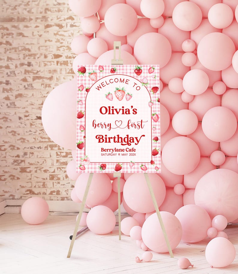 May include: Welcome to Olivia's berry first Birthday sign with a pink and white gingham background and red strawberries. The sign is on a wooden easel.