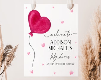 May include: A white sign with pink hearts and a pink heart-shaped balloon. The sign says "Welcome to Addison Michael's Baby Shower Saturday 11th February".