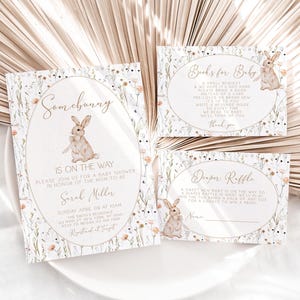 May include: Baby shower invitation set with a floral design and a bunny illustration. The invitation reads "Somebunny is on the way" and includes details for the event. Additional cards include "Books for Baby" and "Diaper Raffle".