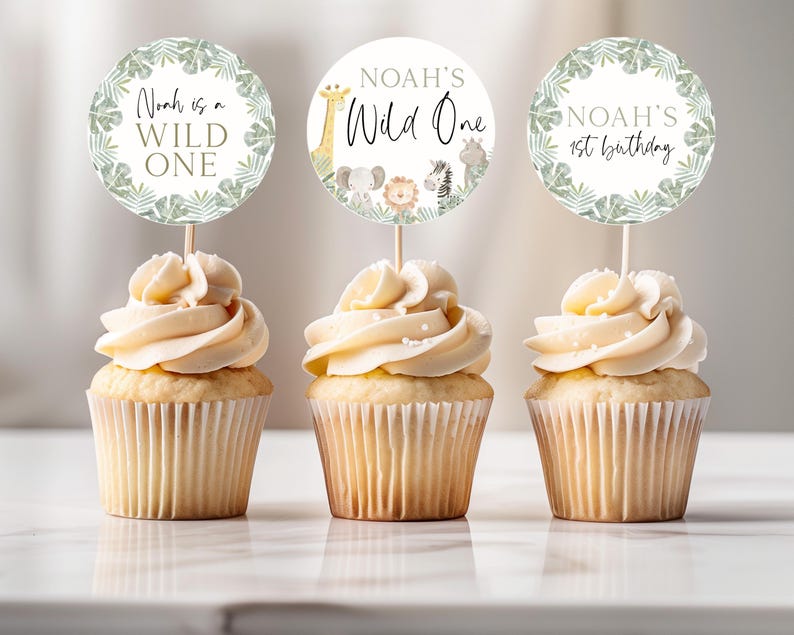 May include: Three cupcakes with white frosting and green and gold animal-themed cupcake toppers. The toppers say "Noah is a Wild One", "Noah's Wild One", and "Noah's 1st Birthday".