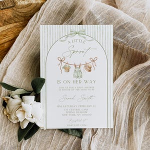 May include: Baby shower invitation with a green and white striped background. The invitation features the text "A Little Sprout Is On Her Way" and includes details for the event. A floral arrangement and fabric are in the background.