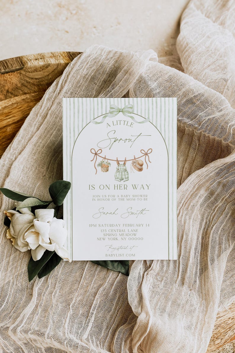 May include: Baby shower invitation with a green and white striped background. The invitation features the text "A Little Sprout Is On Her Way" and includes details for the event. A floral arrangement and fabric are in the background.