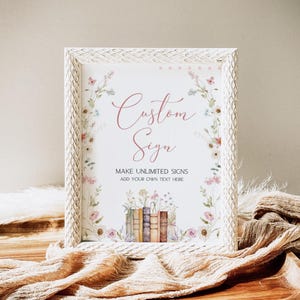 May include: A framed sign with the words "Custom Sign" in a cursive font. The sign is decorated with floral illustrations and a stack of books. The frame is white with a textured pattern. The text "MAKE UNLIMITED SIGNS ADD YOUR OWN TEXT HERE" is also on the sign.