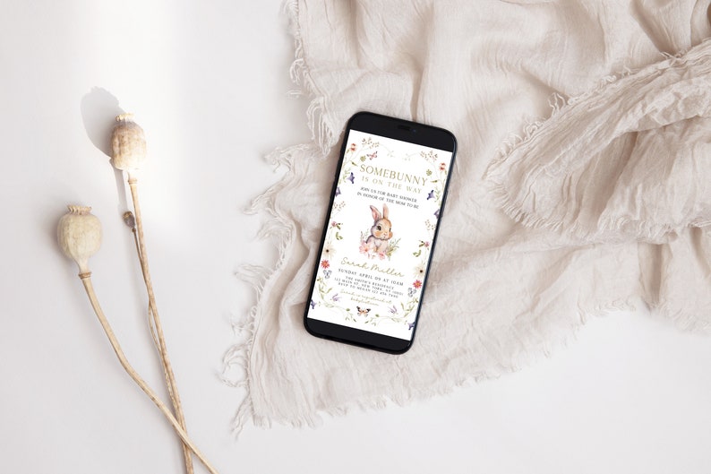 Puede incluir: Un tel&eacute;fono inteligente que muestra una invitaci&oacute;n a una fiesta de bienvenida al beb&eacute; con un borde floral y un conejito de dibujos animados. La invitaci&oacute;n dice "Somebunny is on the way" e incluye la fecha, la hora y el lugar del evento. El texto tambi&eacute;n incluye el nombre "Sarah Miller".