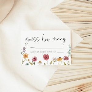 Op de afbeelding: Een witte kaart met de tekst "guess how many" in zwarte cursieve letters. De kaart heeft een bloemige rand met aquarelbloemen in tinten roze, geel, oranje en blauw. De kaart heeft twee lege regels voor een naam en het aantal snoepjes in een pot.