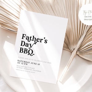 May include: A white Father's Day BBQ invitation with black text. The invitation includes the date, time, and location details. The invitation is placed on a white plate with a dried palm leaf.