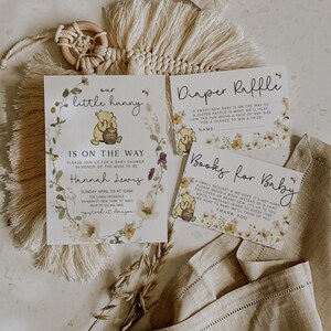 May include: A Winnie the Pooh themed baby shower invitation with floral accents. The invitation includes the text "our little hunny is on the way".