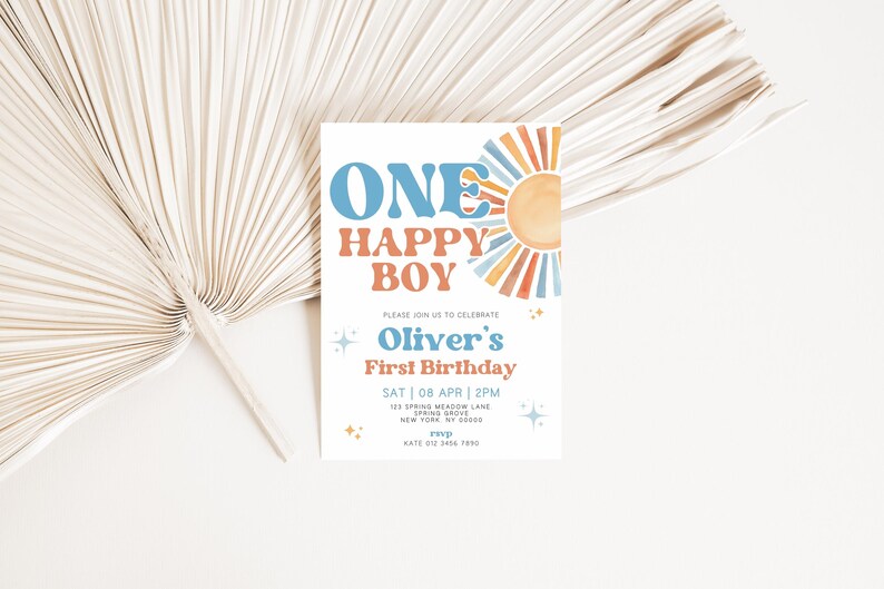以下が含まれることがあります： 青とオレンジ色の「ONE HAPPY BOY」の文字と水彩画の太陽のイラストが描かれた白い招待状。カードには「Oliver's First Birthday」と日付と時間の詳細が記載されています。背景には、乾燥したヤシの葉の扇子があります。