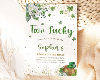 Pode incluir: Um cartão branco com trevos verdes e glitter dourado. O texto diz "Two Lucky" e "Sophia's Second Birthday". O cartão também inclui a data, a hora e o local da festa, bem como um contato para RSVP.