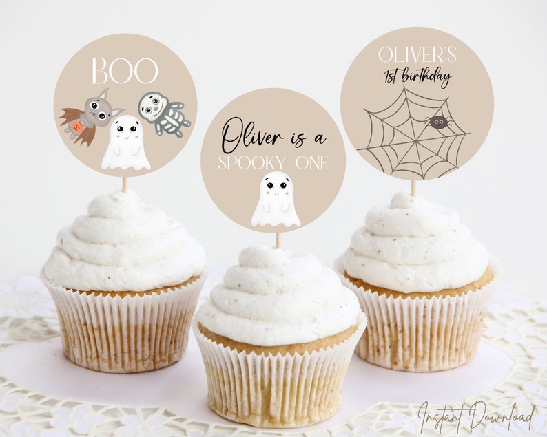 Puede incluir: Tres cupcakes con adornos beige con dise&ntilde;os de Halloween. Uno dice "BOO" con un murci&eacute;lago, un fantasma y un esqueleto. Otro dice "Oliver is a spooky one" con un fantasma. El tercero dice "Oliver's 1st birthday" con una ara&ntilde;a y una telara&ntilde;a.