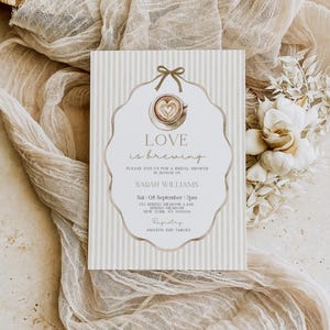 May include: Bridal shower invitation with a coffee cup design and the words "Love is brewing." The invitation has a beige and white striped background and includes the name Sarah Williams, date, time, and location.