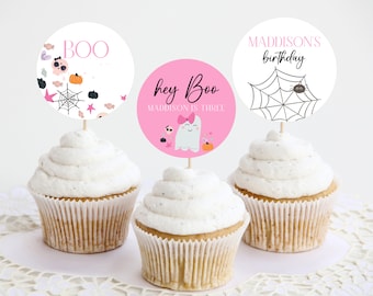 May include: Three pink and white cupcake toppers with Halloween themes. The toppers feature a ghost, a spider web, and a skull and crossbones. The text on the toppers reads "Boo", "Hey Boo Maddison is Three", and "Maddisons birthday".