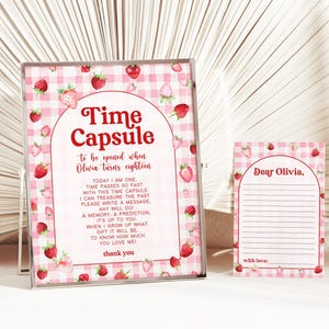 May include: A pink and white gingham time capsule with strawberries and the text "Time Capsule to be opened when Olivia turns eighteen."  The text continues with instructions for writing a message, memory, or prediction for Olivia to read when she turns eighteen.  A separate pink and white gingham card with strawberries says "Dear Olivia." with lines for writing a message.