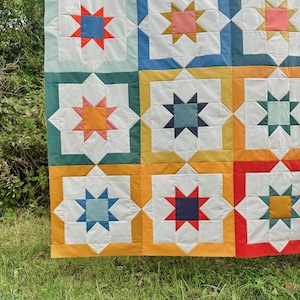 May include: A colorful quilt with a repeating pattern of stars in various colors, including red, blue, yellow, orange, and green. The quilt is made of fabric squares sewn together to create a geometric design.