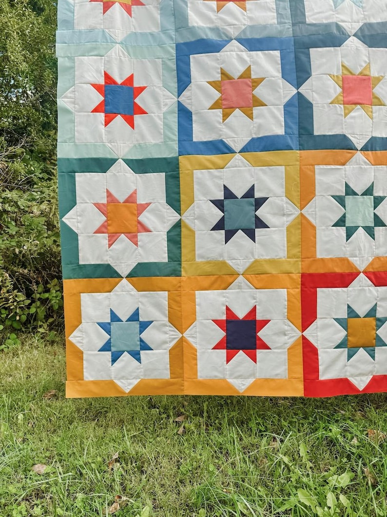 May include: A colorful quilt with a repeating pattern of stars in various colors, including red, blue, yellow, orange, and green. The quilt is made of fabric squares sewn together to create a geometric design.