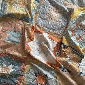 May include: A patchwork quilt with a variety of floral and geometric patterns in shades of blue, orange, and yellow. The quilt is made up of squares and stars, and it is folded in half.