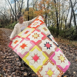 May include: A colorful patchwork quilt with a starburst pattern in shades of pink, yellow, orange, and brown. The quilt is made of various fabrics with different textures and patterns.