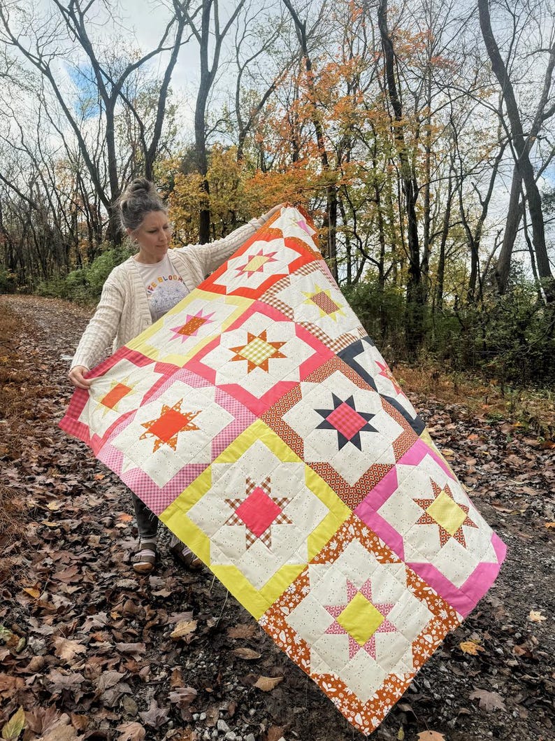 May include: A colorful patchwork quilt with a starburst pattern in shades of pink, yellow, orange, and brown. The quilt is made of various fabrics with different textures and patterns.