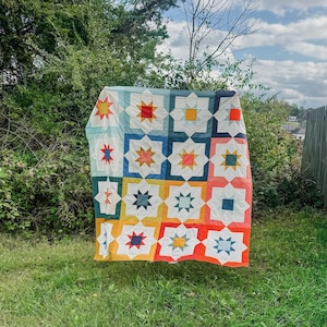 May include: A colorful quilt with a geometric pattern of stars and squares in shades of blue, red, yellow, orange, and white.