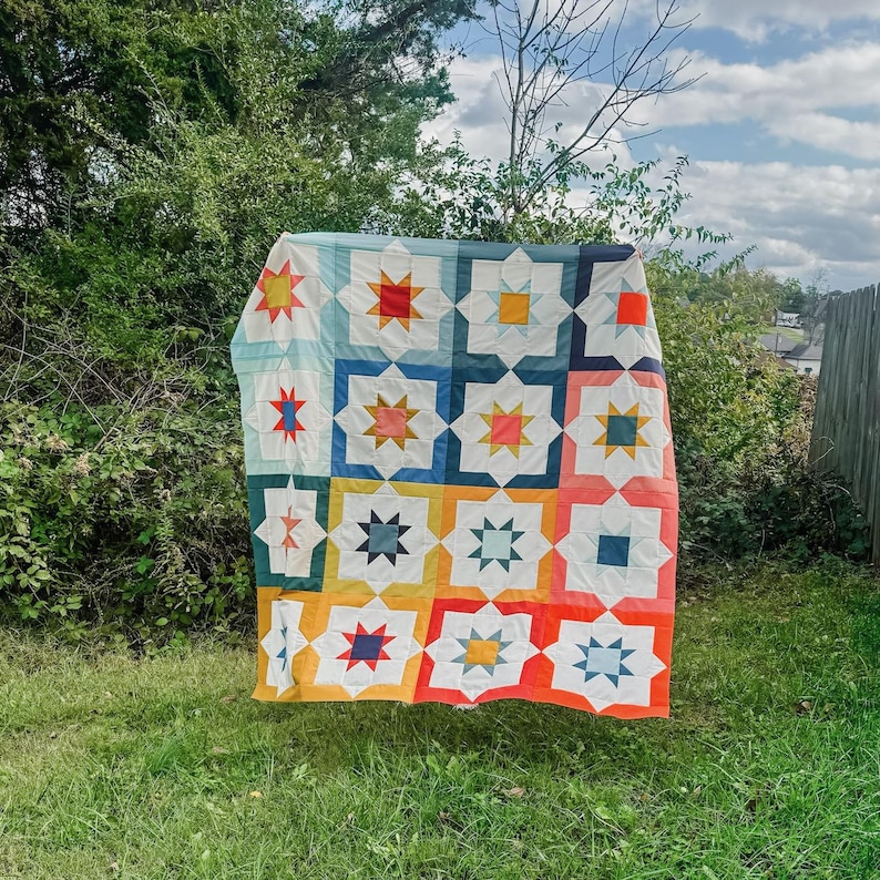 May include: A colorful quilt with a geometric pattern of stars and squares in shades of blue, red, yellow, orange, and white.