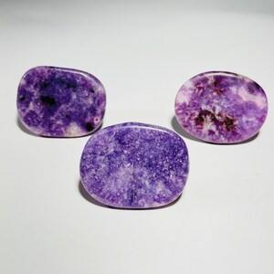 May include: Three purple and white oval-shaped stones with a speckled pattern. The stones are smooth and polished.
