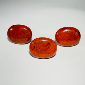 May include: Three smooth, oval-shaped stones with a red-orange base and black marbling.