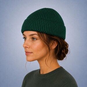 May include: A dark forest green beanie with a thick, ribbed knit texture and a wide, folded cuff. The hat features a classic, close-fitting silhouette that sits snugly on the head, showcasing a consistent vertical ribbed pattern throughout.