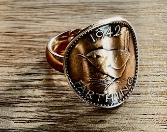 Op de afbeelding: Koperkleurige ring met een Farthing-munt uit 1942. De munt toont een vogel en de tekst 'Farthing'. De ring heeft een eenvoudige band en een gepolijste afwerking. De diameter van de munt is ongeveer 2,5 cm.